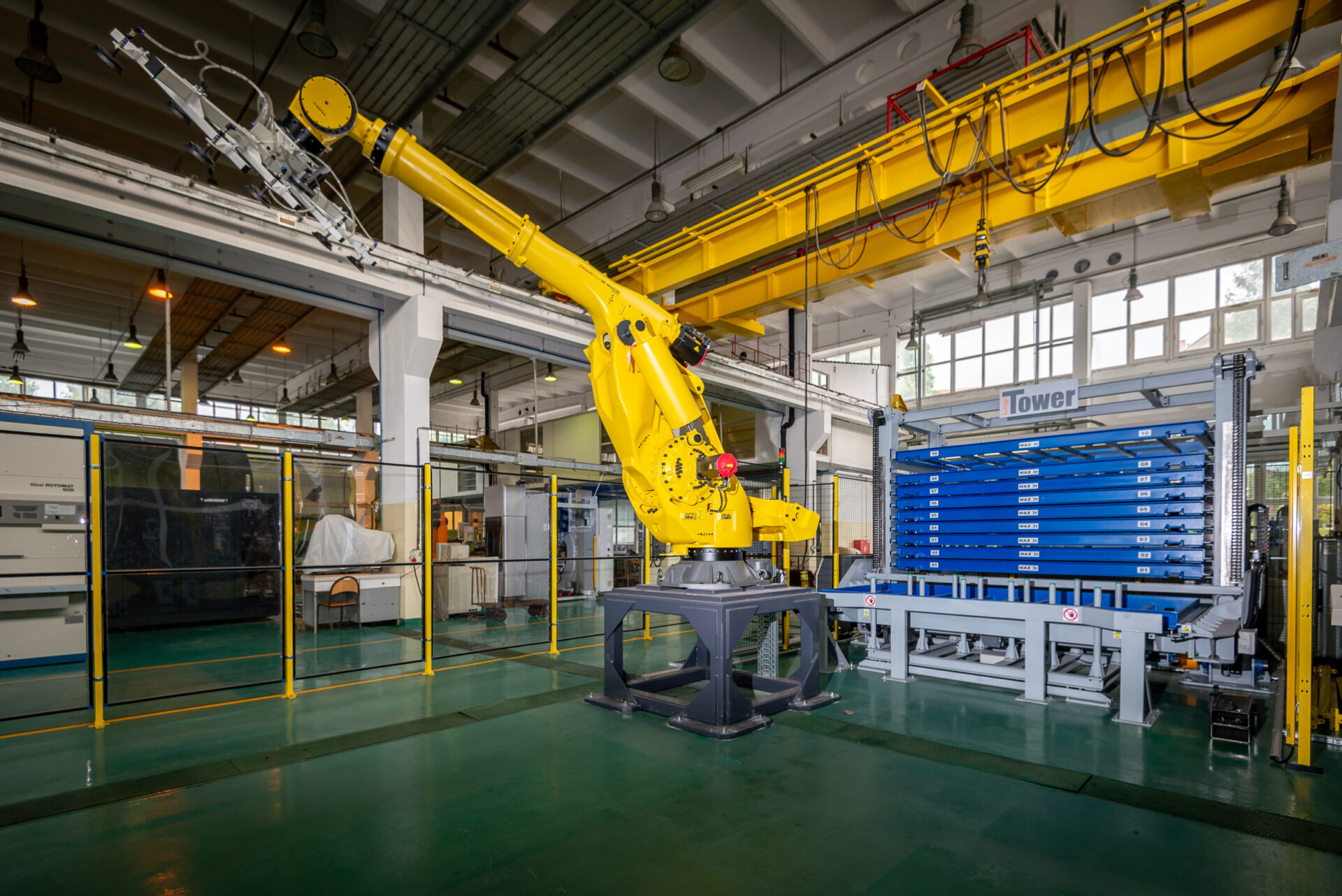 Aparatura znajdująca się w pracowni E-Produkcji. Zdjęcie przedstawia zrobotyzowane gniazdo produkcyjne, w którego skład wchodzą: magazyn blach, robot o udźwigu 400kg oraz wycinarka laserowa.